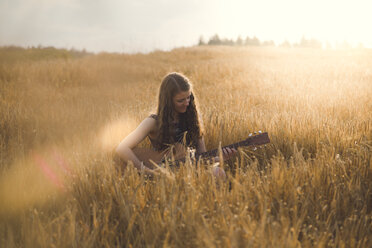 Junge Frau spielt abends auf einem Feld Gitarre - SARF002053