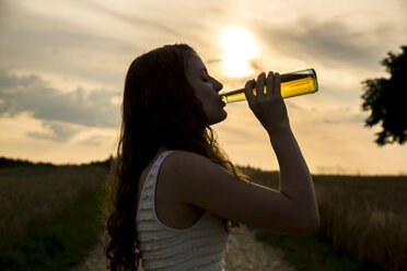 Junge Frau trinkt aus Glasflasche, Abendsonne - SARF002041