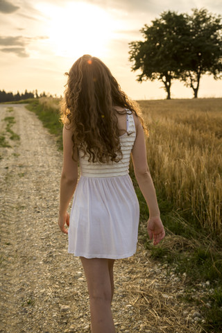 Junge Frau geht auf einem Feldweg, Abendsonne, lizenzfreies Stockfoto