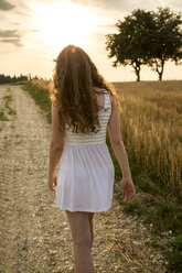 Young woman walking on field path, evening sun - SARF002056
