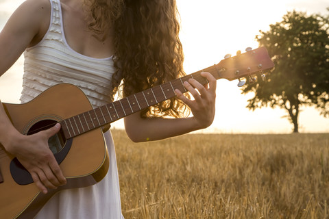 Junge Frau spielt Gitarre, Abendsonne, Gerstenfeld, lizenzfreies Stockfoto