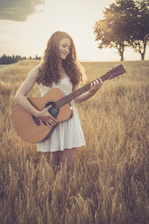 Junge Frau spielt Gitarre auf einem Feld, am Abend - SARF002042