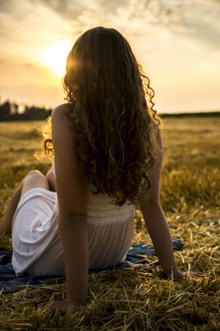 Junge Frau sitzt abends auf einem Feld, lizenzfreies Stockfoto