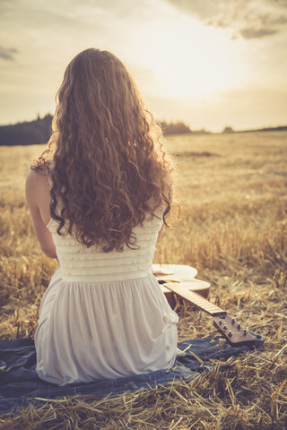Junge Frau sitzt abends auf einem Gerstenfeld, lizenzfreies Stockfoto