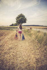 Junge Frau mit Gitarre auf einem Feld, am Abend - SARF002051