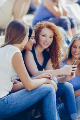 Portrait of teenage girl with a mobile phone sitting amongst her female friends - CHAF000793