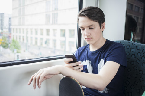 Jugendlicher mit Skateboard, der in der S-Bahn sitzt und sein Smartphone benutzt, lizenzfreies Stockfoto