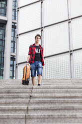 Germany, Berlin, teenage boy with suitcase walking downstairs - MMFF000859