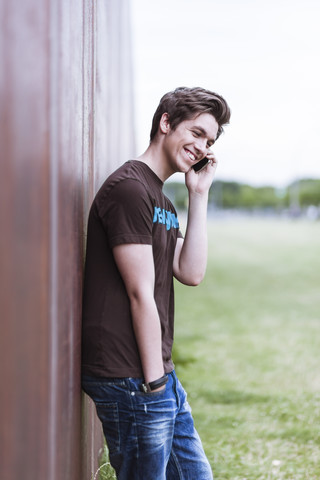 Telephoning teenage boy leaning on corten wall stock photo