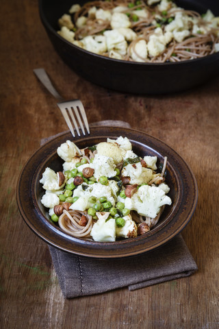 Gericht aus Dinkelvollkornspaghetti mit geröstetem Blumenkohl, Haselnüssen, Erbsen und Basilikum, lizenzfreies Stockfoto