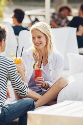 Porträt einer glücklichen jungen Frau mit einem Glas frischen Saft, die mit ihrem Freund in einem Straßencafé sitzt - CHAF000810