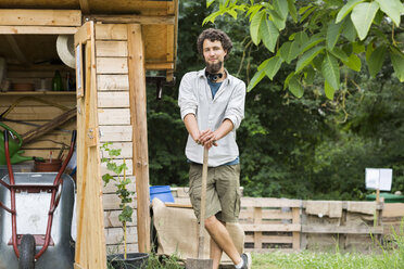 Young man standing in an urban garden leaning on a spade - SGF001763