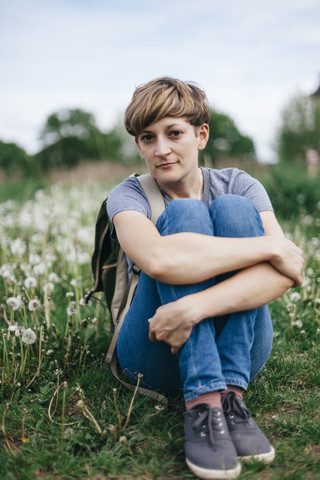 Porträt einer jungen Frau, die auf einer Wiese sitzt und die Knie umarmt, lizenzfreies Stockfoto