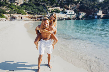 Spain, Majorca, man piggybacking his girlfriend at the sea - CHAF000660