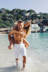 Spain, Majorca, man piggybacking his girlfriend at the sea - CHAF000661