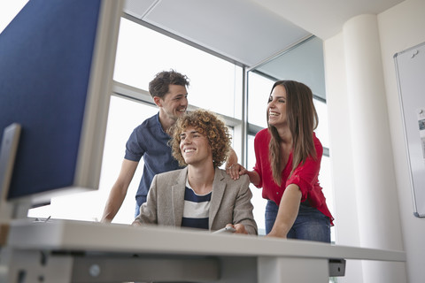 Drei lächelnde Kollegen am Bürotisch, lizenzfreies Stockfoto