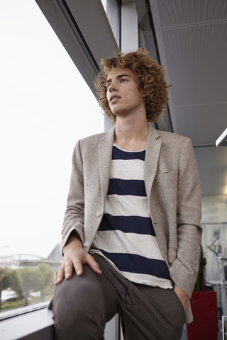 Junger Mann mit lockigem Haar schaut aus dem Fenster, lizenzfreies Stockfoto