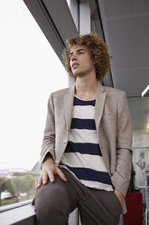 Young man with curly hair looking out of window - RHF000920