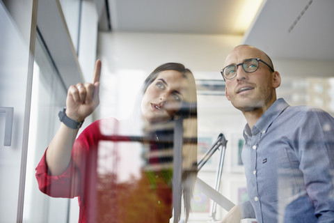 Mann und Frau in einem Büro, die hinter einer Glasscheibe diskutieren, lizenzfreies Stockfoto