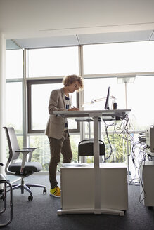 Junger Mann im Büro bei der Arbeit an einem verstellbaren Schreibtisch - RHF000933
