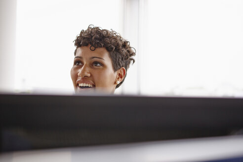 Lächelnde junge Frau in einem Büro hinter einem Computerbildschirm - RHF000938