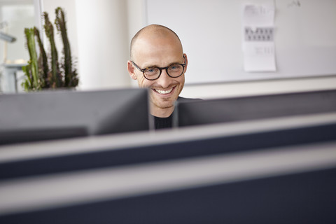 Lächelnder Mann im Büro hinter Computerbildschirmen, lizenzfreies Stockfoto