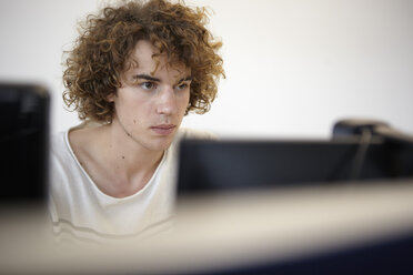 Junger Mann im Büro mit Blick auf den Computerbildschirm - RHF000956