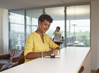 Young woman in office writing in notebook - RHF000971