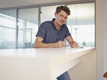 Junger Mann im Büro beim Schreiben am Schalter - RHF000972