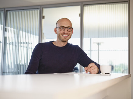 Lächelnder Mann im Büro beim Schreiben am Schalter - RHF000974