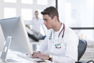 Doctor sitting at desk working on computer - ZEF006041