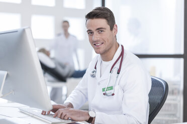 Portrait of smiling doctor sitting at desk working on computer - ZEF006042