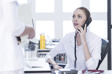 Krankenschwester am Schreibtisch am Telefon mit Blick auf den Arzt - ZEF006749