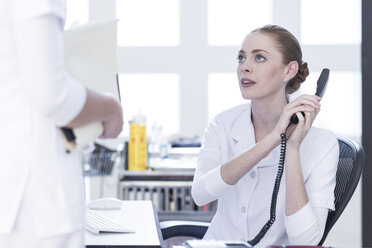 Krankenschwester am Schreibtisch am Telefon mit Blick auf den Arzt - ZEF006049