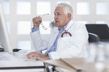 Senior doctor sitting at desk working on computer - ZEF006052