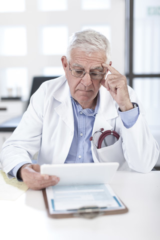 Seriöser Oberarzt am Schreibtisch mit Blick auf die Patientenakte, lizenzfreies Stockfoto