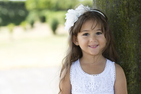 Portrait of smiling little girl leaning on a tree - GDF000811