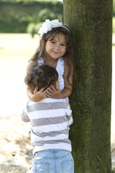 Porträt eines lächelnden Mädchens, das sich an einen Baum lehnt und seinen kleinen Bruder umarmt - GDF000812