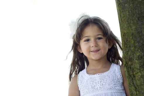Porträt eines lächelnden kleinen Mädchens, das sich an einen Baum lehnt - GDF000813