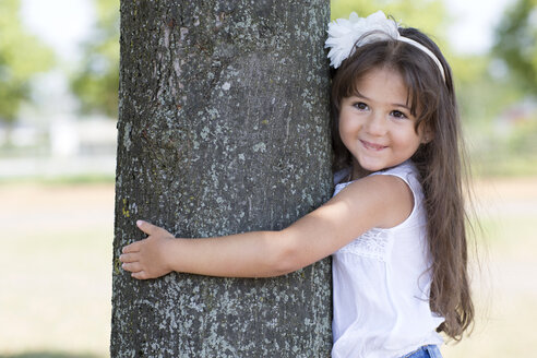 Portrait of smiling little girl hugging a tree - GDF000814