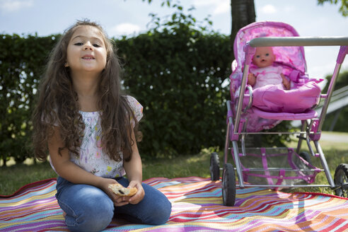 Little girl sitting on a blanket besides her doll buggy - GDF000820