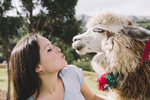 Peru, Cusco, junge Frau, die einem Alpaka gegenübersteht, lizenzfreies Stockfoto