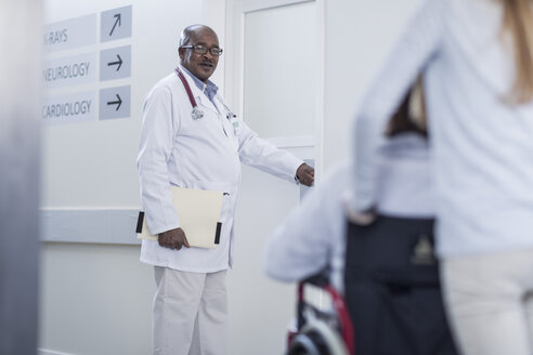 Arzt im Krankenhauskorridor öffnet Tür und Patient im Rollstuhl - ZEF006818
