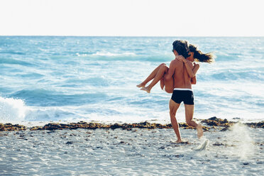 USA, Miami, young man carrying his girlfriend and running into the sea - CHAF000831