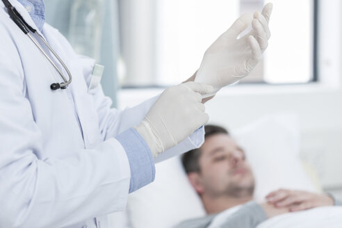 Arzt zieht Handschuhe an, Patient im Hintergrund - ZEF006529