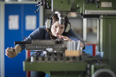 Junge Frau mit Gehörschutz bei der Arbeit an einer Maschine - SGF001744