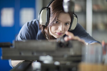 Junge Frau mit Gehörschutz bei der Arbeit an einer Maschine - SGF001745