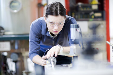 Junge Frau mit Schutzbrille bei der Arbeit an einer Maschine - SGF001775