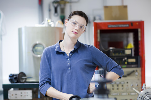 Porträt einer jungen Frau mit Schutzbrille in einer Werkstatt, lizenzfreies Stockfoto