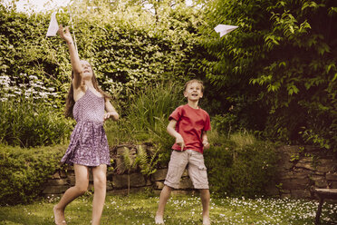 Mädchen und Junge spielen mit Papierfliegern im Garten - MFF001875